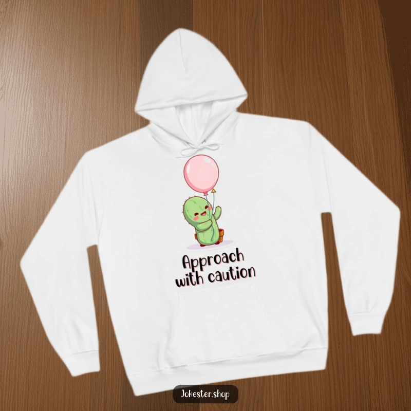 Funny cactus character comically attempting to hug a balloon, featured on a cozy hoodie, depicting a humorous and heartwarming effort.